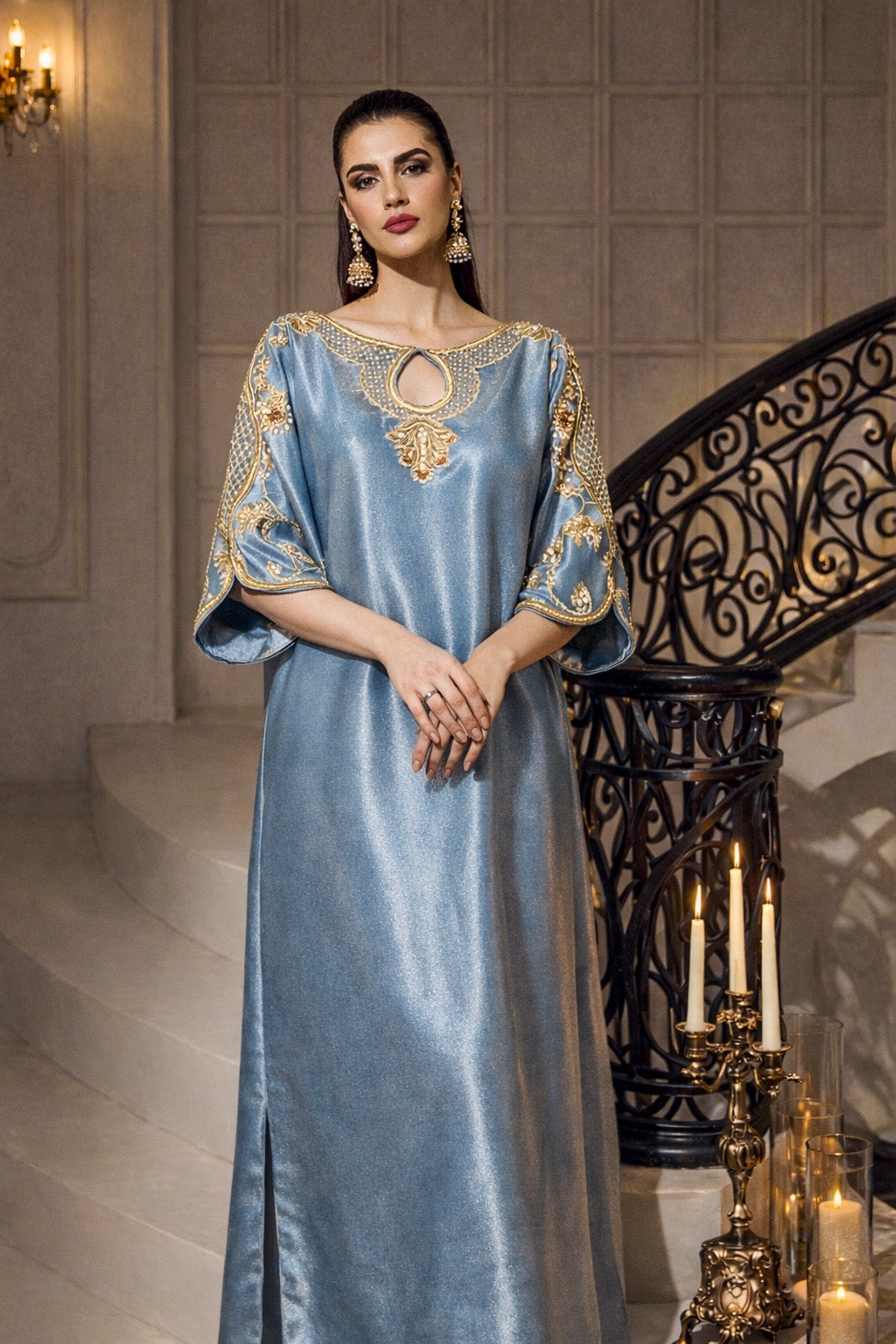 Woman in a blue evening gown with gold embroidery standing in an elegant interior setting.
