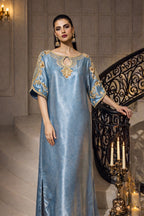Woman in a blue dress with gold embroidery standing in an elegant interior setting.