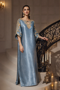 Woman in a blue evening gown with gold embroidery standing in an elegant interior setting.