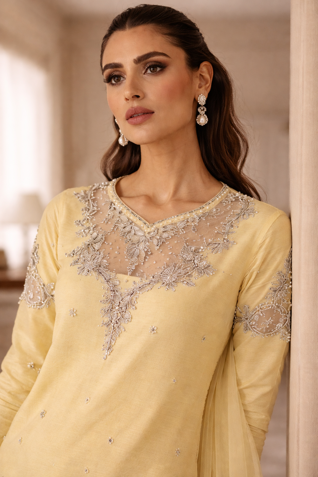 Woman wearing a light yellow dress with intricate silver embroidery indoors.