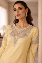 Woman wearing a light yellow dress with intricate silver embroidery indoors.