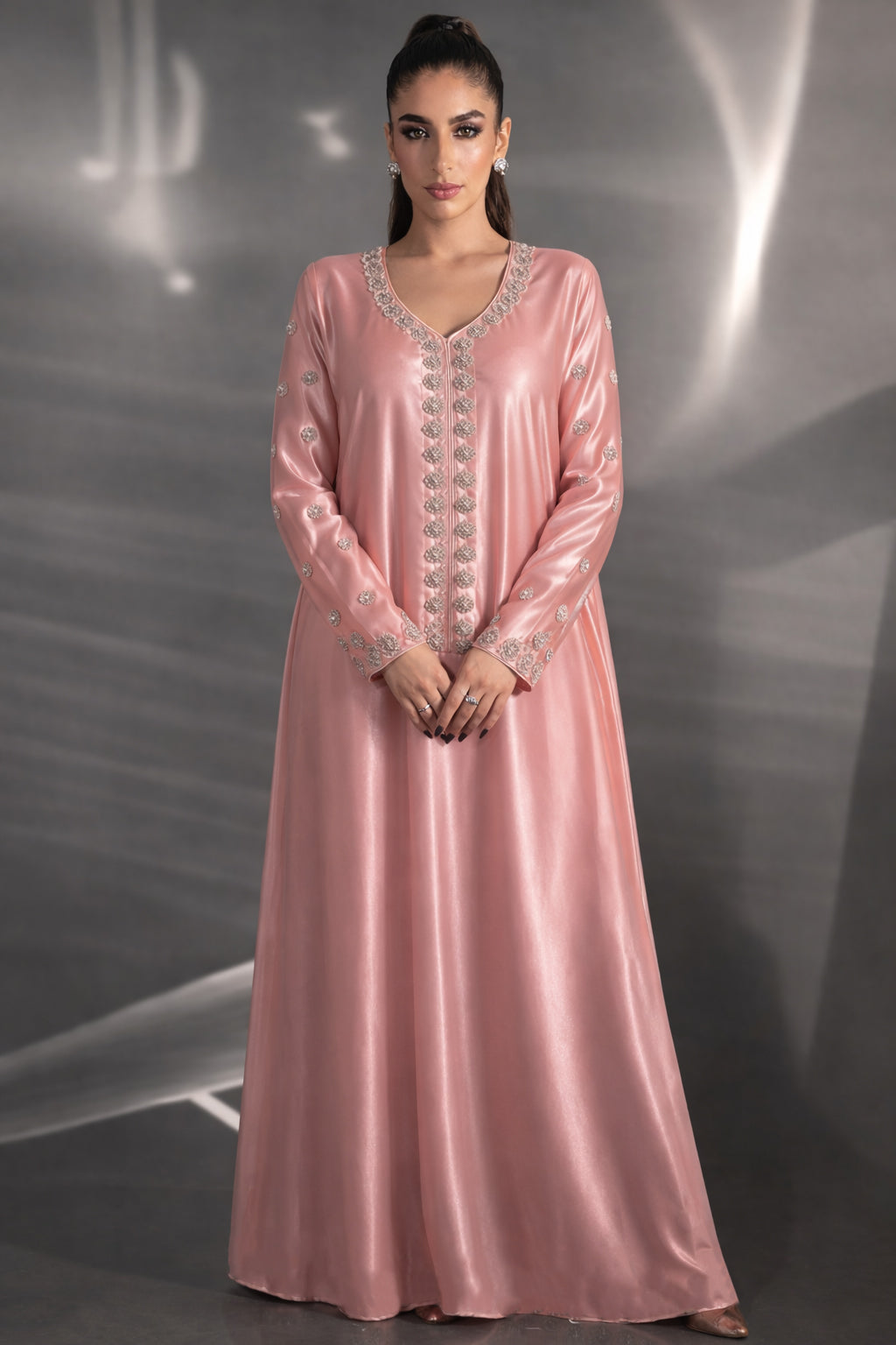 Woman wearing a pink evening gown with intricate detailing against a gray background