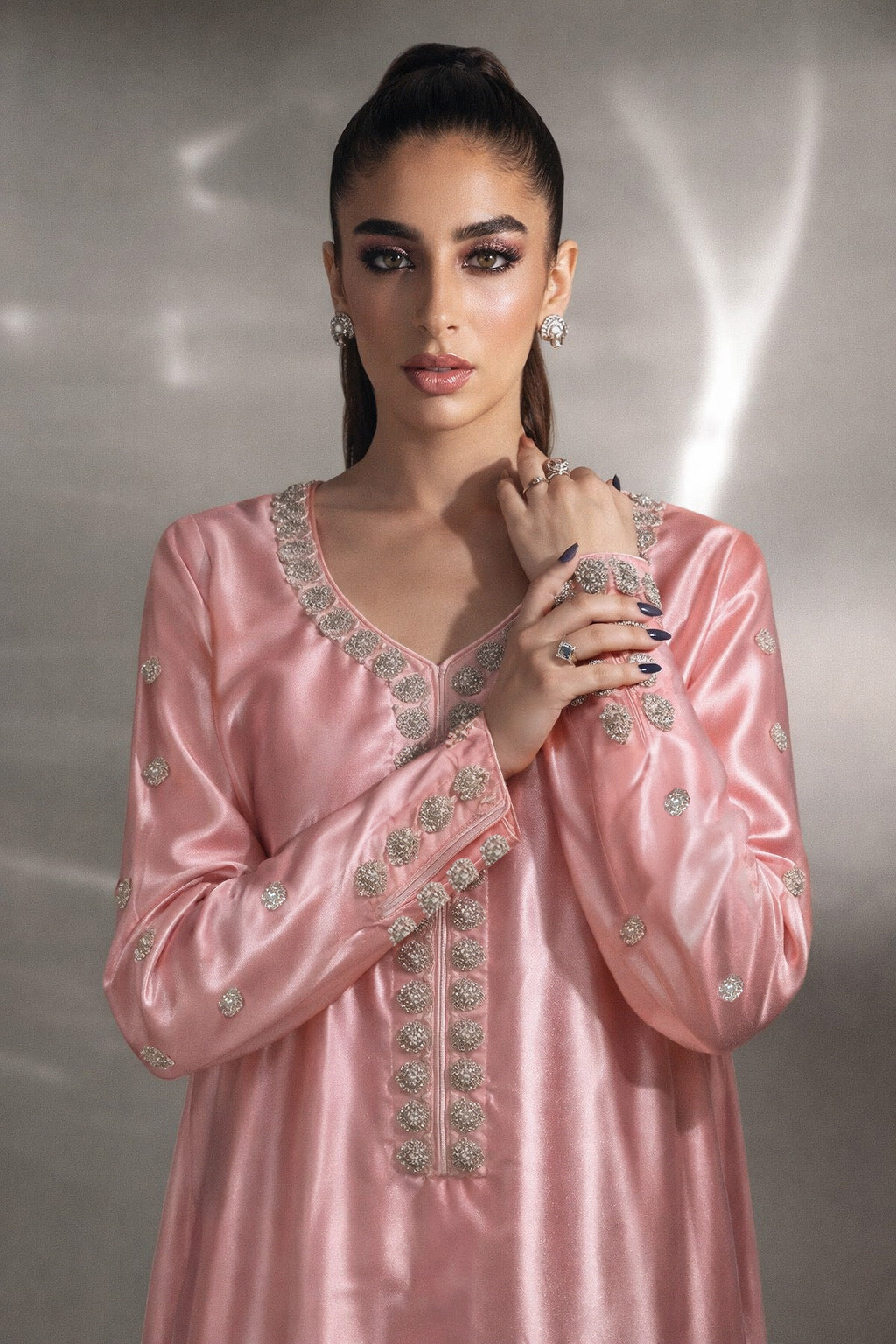 Woman wearing a pink traditional outfit with intricate designs against a neutral background