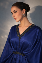 Woman wearing a blue dress with intricate detailing against a neutral background