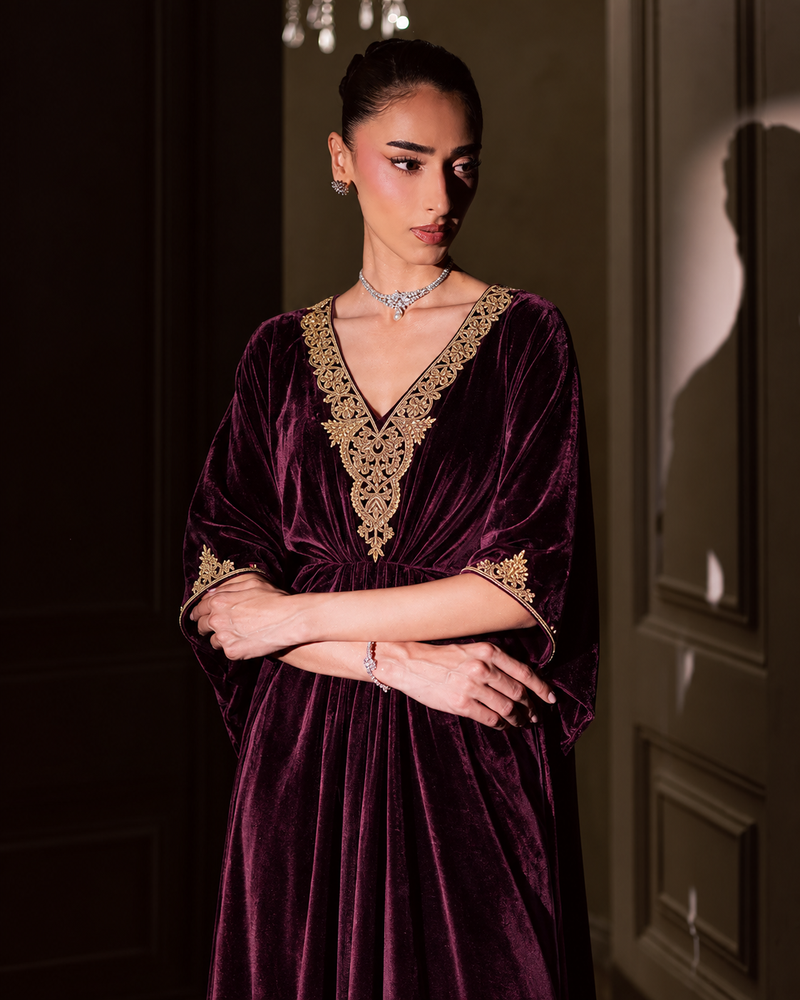 Zohra wine velvet kaftan with gold embroidered neckline, styled with arms crossed